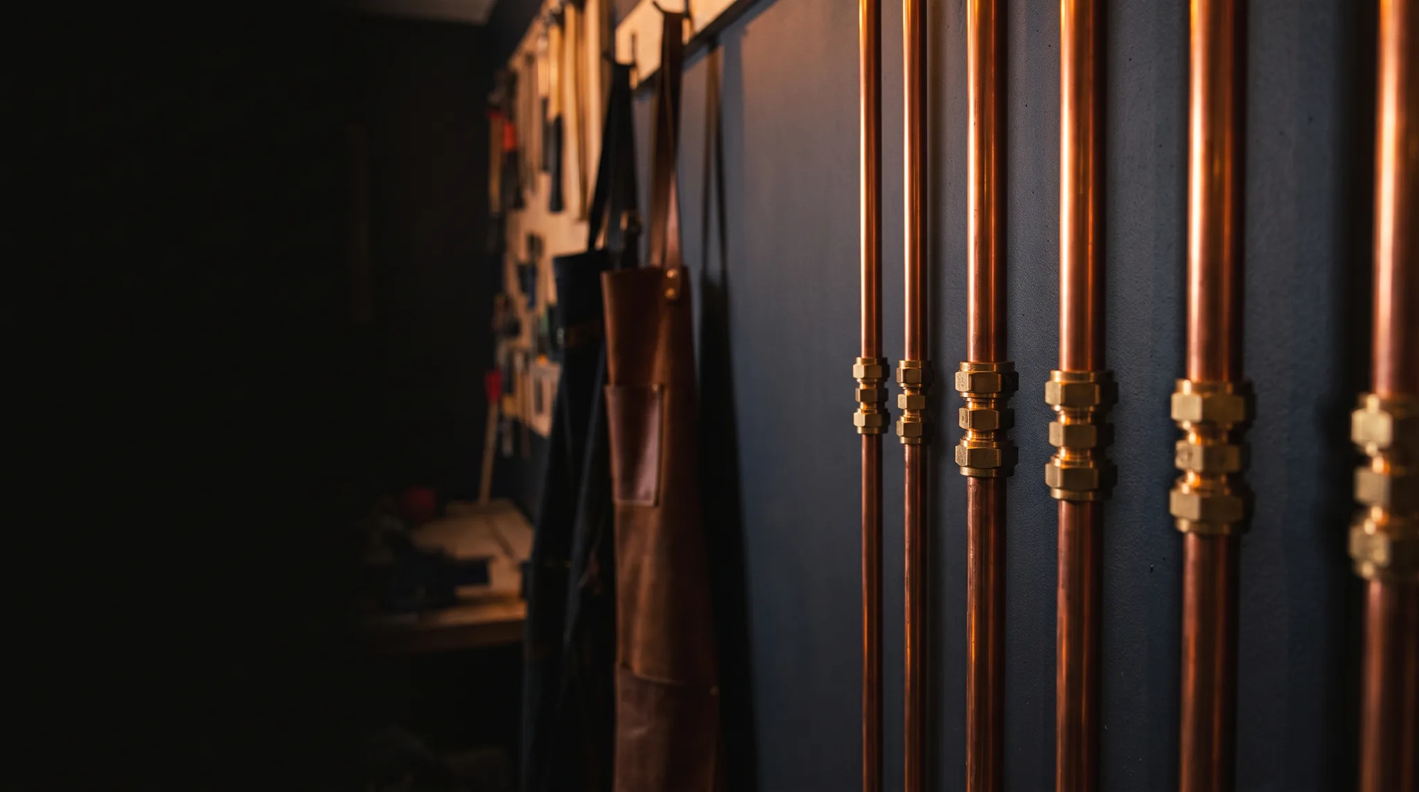 Copper pipework catching warm light against a dark wall, Copperline Plumbing Co.